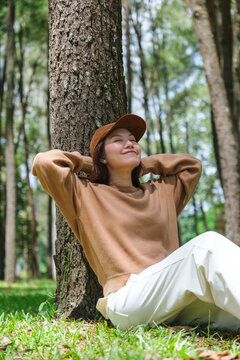 Vertical portrait image of a woman sitting and putting hands behind her neck for relaxing in the park