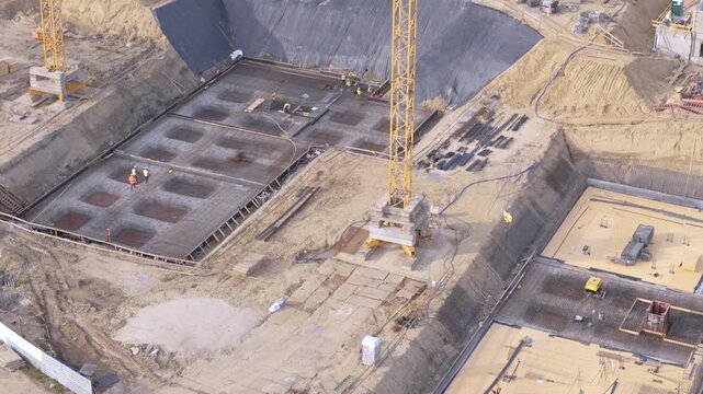 Construction site aerial view featuring building foundation work, tower crane, and workers in deep excavation pit
