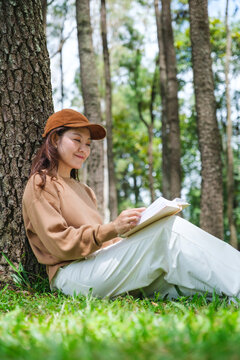 Vertical portrait image of a woman reading a book while sitting in the park