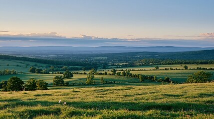 Obraz premium Golden Hour Sunlight Illuminates Rolling Green Hills and Distant Mountains in a Serene Countryside Landscape