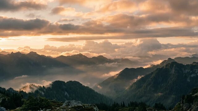 Golden sunbeams illuminate mountain valley while clouds drift softly across rugged alpine ridges during majestic sunset. Serene wilderness scenery evokes feelings of peace and tranquility.