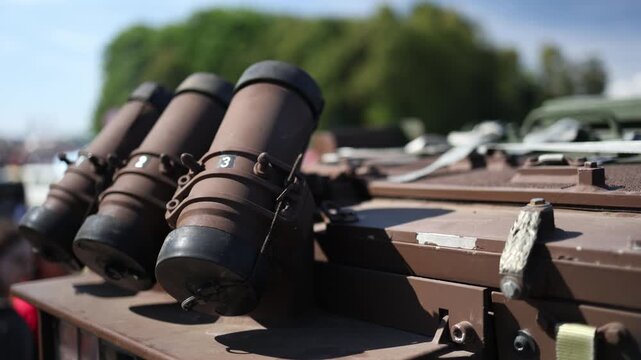 Closeup of smoke grenade launchers mounted on armored military vehicle shows three protective countermeasure tubes and durable equipment during outdoor defense exhibition