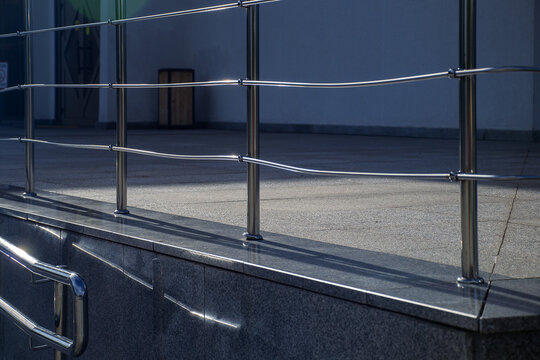 Shiny stainless steel handrails and protective barriers mounted on stone tile terrace of a public building