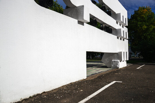 Modern white concrete building facade with massive geometric structural elements standing next to asphalt road under blue sky with copy space