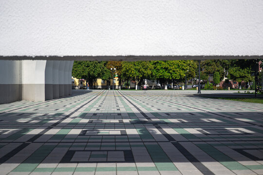 View through geometric concrete building structure on empty public square with green and grey tiled pavement and copy space