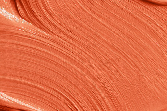 Orange cream smudge with wavy lines forming a textured abstract background, ideal for cosmetic product presentations and beauty themes