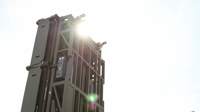 Air defense missile launcher rises into bright sunlight with tall launch canisters and heavy tactical frame creating a dramatic military silhouette against clear blue sky