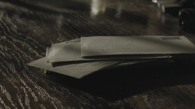 Stack of brown stamped envelopes scattered across a dark tabletop in dramatic low light, creating a retro communication concept associated with payment demands.