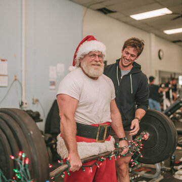 Muscular Santa Claus in a weightlifting gym with a spotter