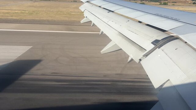 A passenger window view showing an airplane wing and flaps during landing on a sunny runway. Ideal for travel, aviation, and transportation themes.