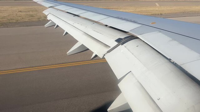 A closeup view from a passenger window showing the mechanical movement of airplane wing flaps and spoilers during a landing sequence on an airport runway.