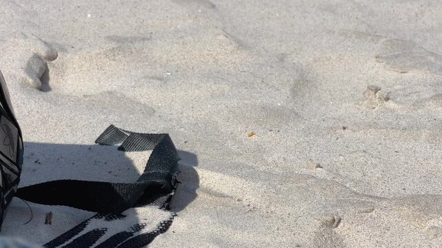A detailed closeup shot of a black nylon bag strap resting on soft white sand. Useful for travel, vacation, and minimalist lifestyle themes.