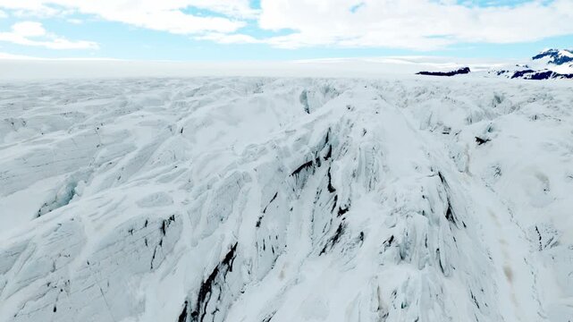 Fjallsjokull glacier shows broad snow-covered ice and deep crevasses around a rugged ridge on Vatnajokull in southeast Iceland, captured during a drone forward flyover.