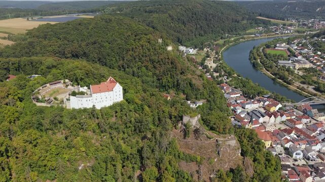 Drone view of Rosenburg Castle on a rocky wooded hill over the town of Riedenburg, Bavaria, with the Altmuhl River and red roofs in the valley below.