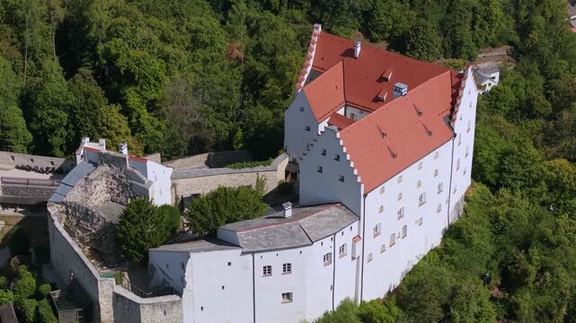 High angle close drone shot of the white keep, stepped gable and red tiled roofs of Rosenburg Castle, a medieval fortress above Riedenburg in Germany.