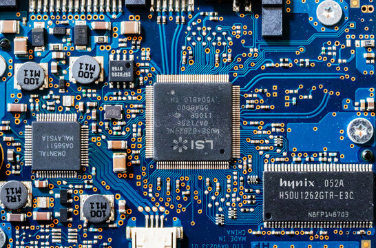 Detailed close-up of a blue printed circuit board featuring branded microchips, capacitors, and soldered components