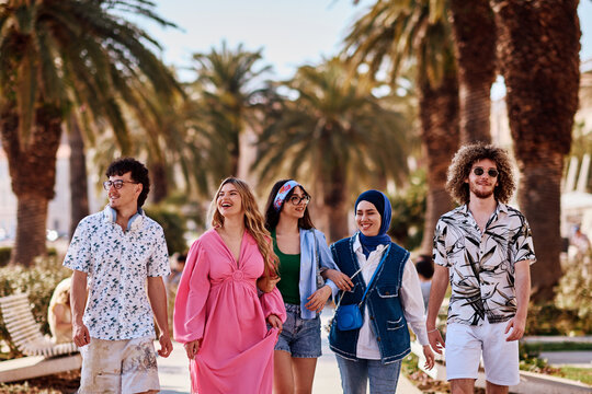 Diverse Group Of Young Friends Walking And Laughing Under Palm Trees On A Sunny Summer Day
