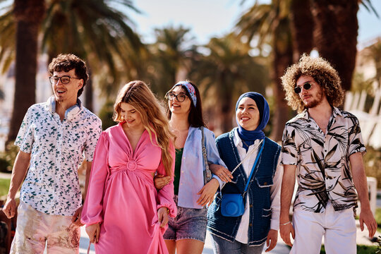 Diverse Group Of Friends Walking Together Along Palm-Lined Promenade On Sunny Summer Day
