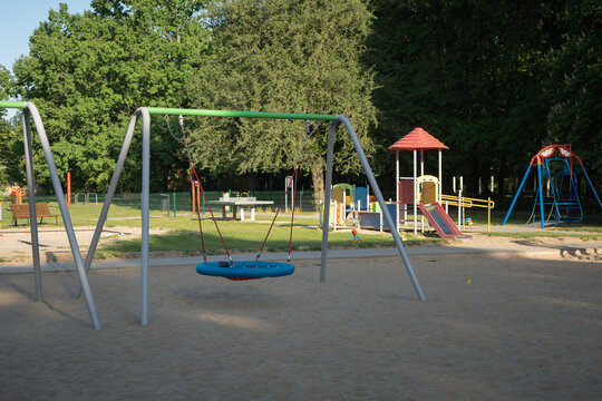 Nest swing stands on sand at empty children playground in public park. Outdoor recreation area provides urban equipment for family leisure, childcare infrastructure and real estate development.