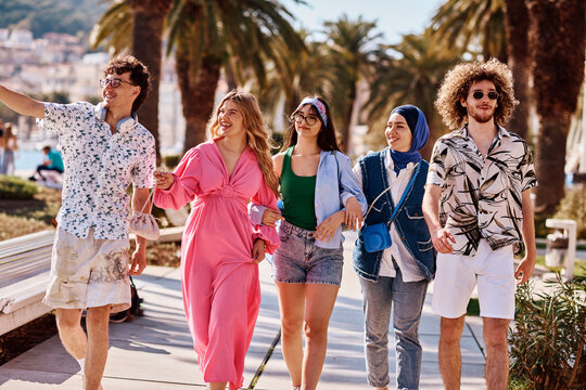 Young Diverse Friends Walking Along Sunny Coastal Promenade With Palm Trees And Laughter