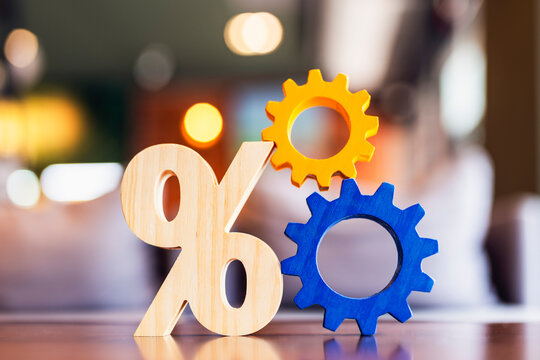 Economic mechanism and monetary policy concept, wooden percentage symbol interlocked with colorful orange and blue gears on table, symbolizing interest rate system, and financial workflow.