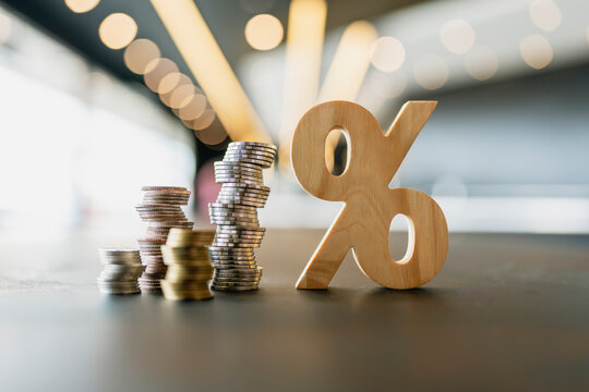 Interest rate increase and investment growth concept, wooden percentage sign beside ascending stacks of coins on modern table, representing bank deposit yield, capital savings, and finance.