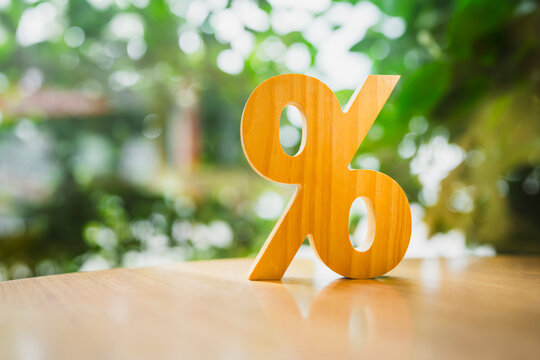 Interest rate and financial yield concept, wooden percentage sign standing on desk against sunny green bokeh garden background, symbolizing discount promotion, commission, and loan return.