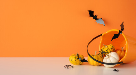 Obraz premium Happy Halloween scene with pumpkin, spider and bat spilling from orange bucket on orange background with empty space