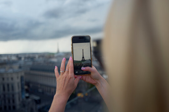 Woman photographs the Eiffel Tower with her phone from a balcony