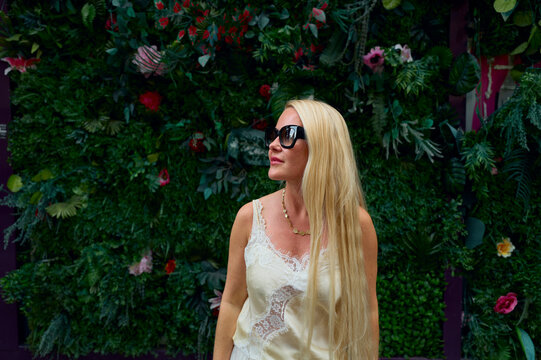 Stylish blonde woman posing by a lush green wall