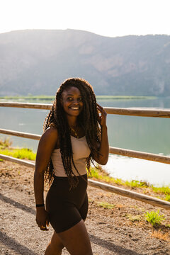 Happy Black woman with long braids walking outdoors by a lake