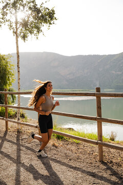 Happy young woman jogging on a path by a lake