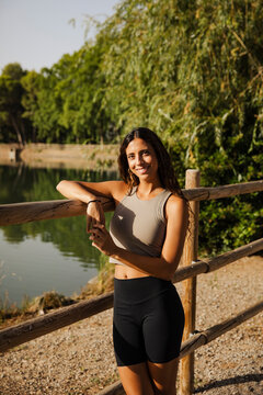 Happy athletic woman leans on a wooden fence outdoors
