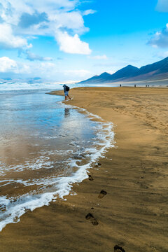 Man walking barefoot along a remote sandy coastline in Fuerteventura