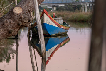 Small colorful wooden boat reflecting in quiet water at sunset © lancho