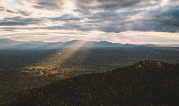 Sunlight breaking through dramatic clouds over forest hills