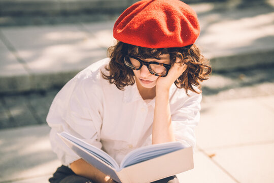 Stylish woman in a red beret reading a book outside on steps