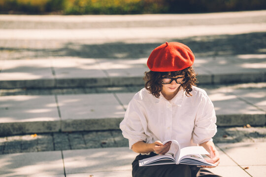 Student in a red beret reads a book on steps on suuny day