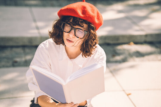 Stylish University student woman reading a book on sunny steps