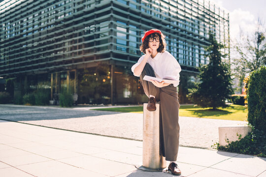Thoughtful young woman with book sitting outside a modern building