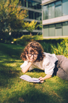 Young woman with glasses reads book on sunny lawn