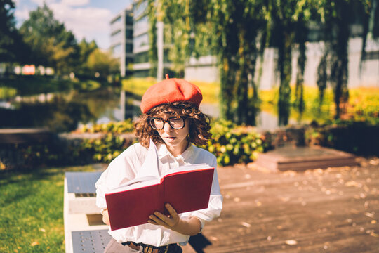 Young stylish woman in red beret reading a book outdoors in a park