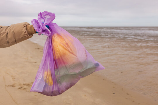 A girl holds a purple garbage bag during a beach cleanup outdoors