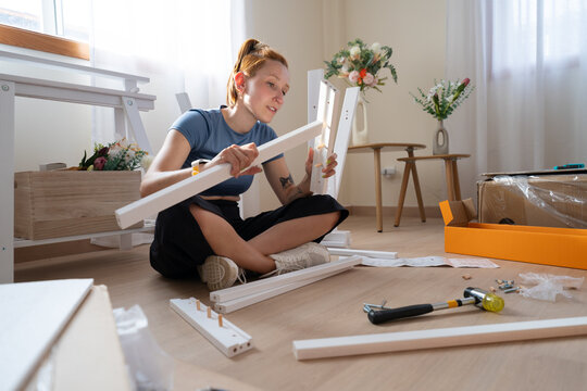 Woman sits on the floor assembling new wooden furniture at home