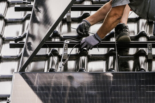 Worker installing a solar panel on a tiled roof outdoors