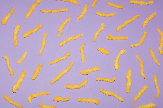 Scattered cheese puffs create a pattern on a purple background