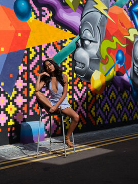 Fashionable woman sits on a stool by a vibrant street art wall