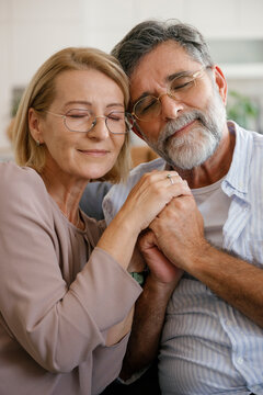 Happy senior couple sitting on sofa holding hands and smiling