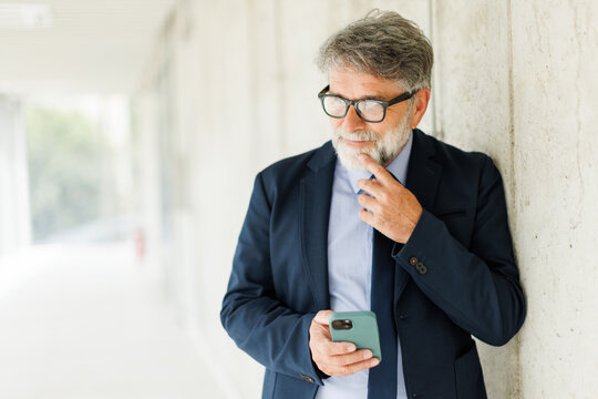 Thoughtful senior businessman holds a smartphone at the office
