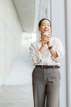 A relaxed businesswoman enjoys a coffee break standing in the office